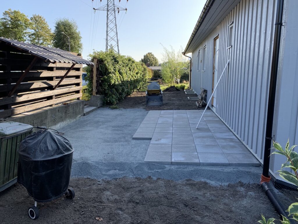 planering med subbus hvor halvparten er dekket med heller paa siden av et hus.