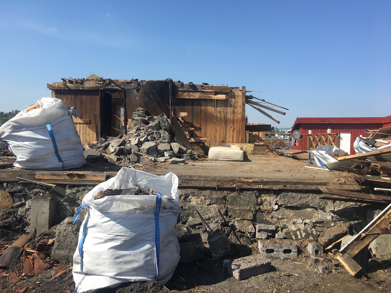 en hytte er delvis revet. Materialer fra riving er plassert i store avfallsbager som straar i front.